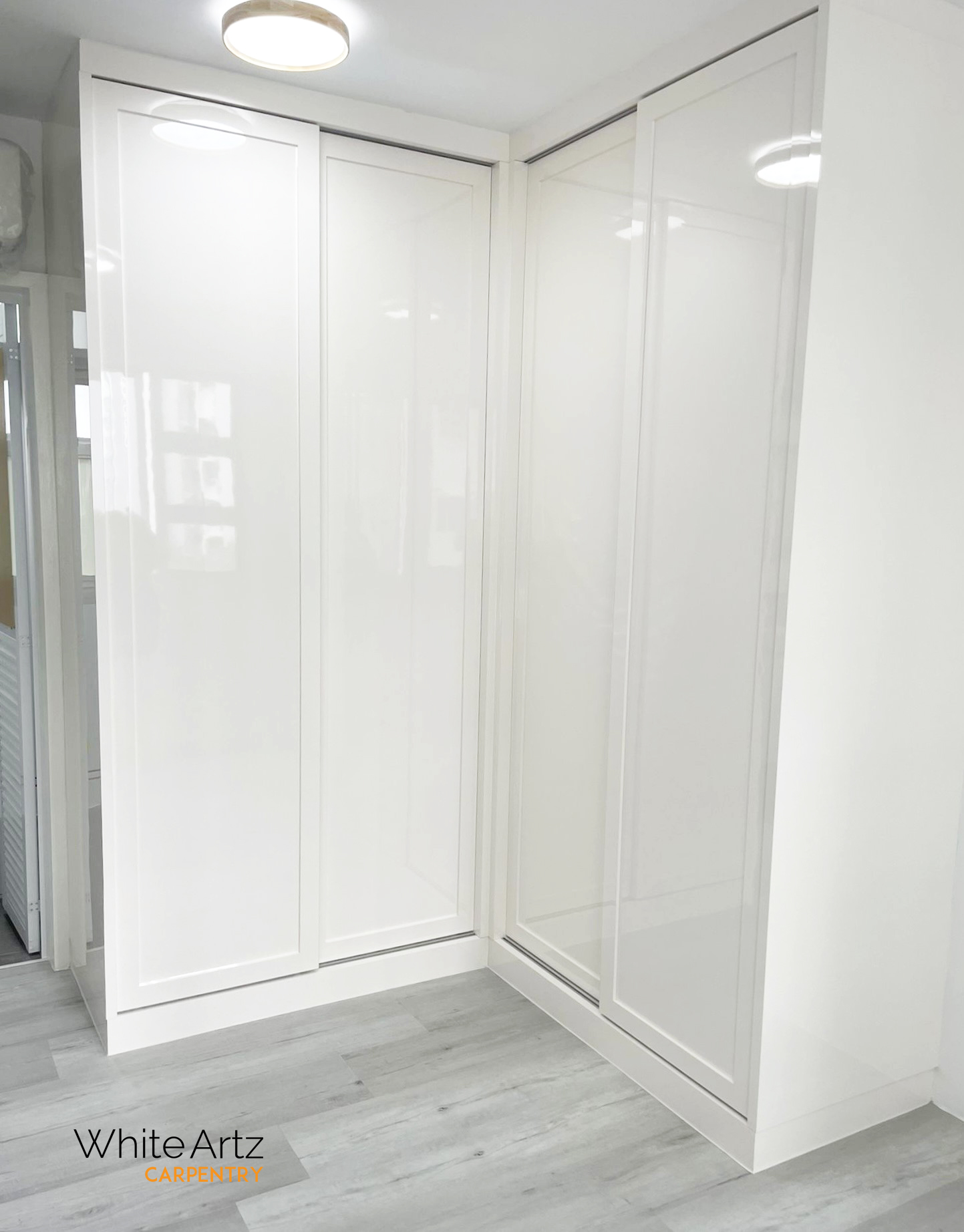 High-gloss white, seamless corner sliding door wardrobe, designed for modern and minimalist spaces by White Artz Carpentry.